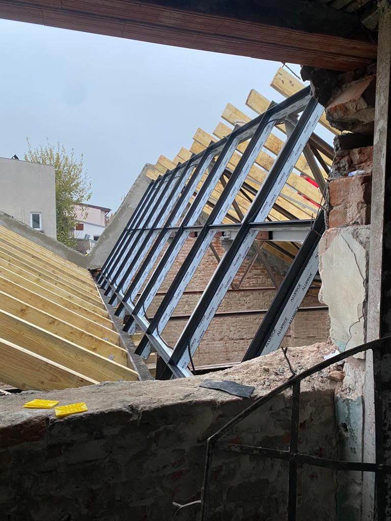 Structura din profile de aluminiu a unui acoperiș vitrat, montată între zidurile din cărămidă și căpriorii din lemn ai unei clădiri vechi