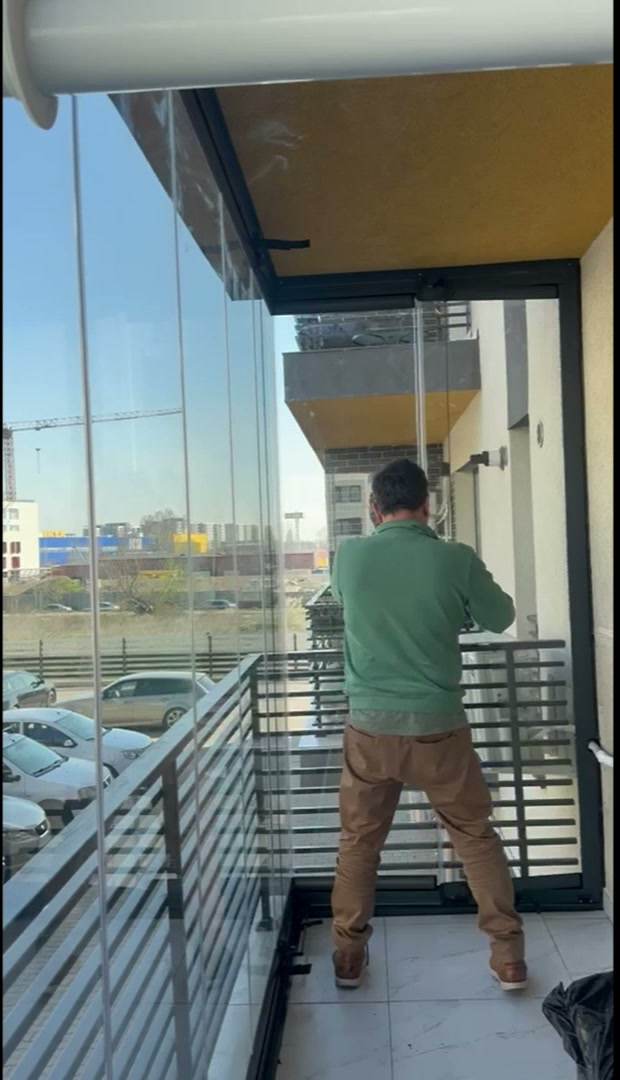 Montator reglând panourile de sticlă armonică în colțul unui balcon cu balustradă metalică