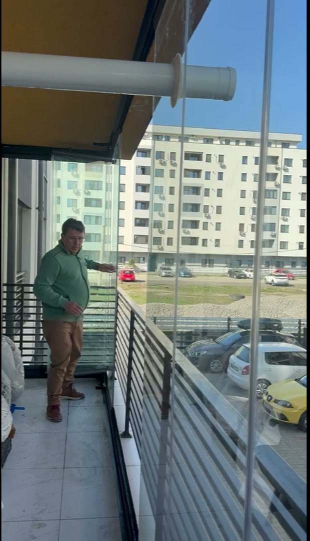 Bărbat lângă un balcon cu sticlă armonică deschisă parțial, cu panou pentru țeava de evacuare a centralei