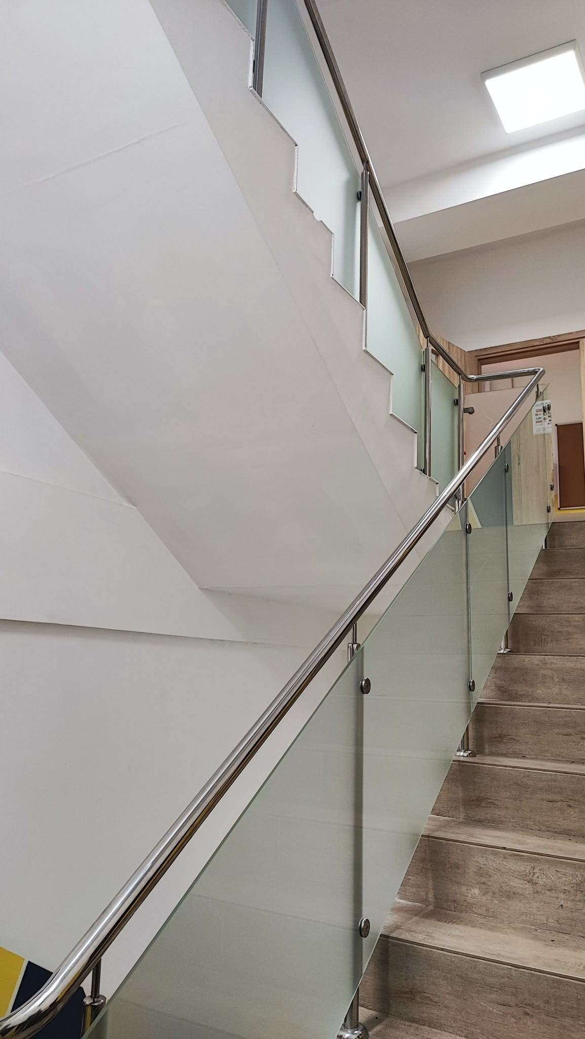 Balustradă din sticlă mată pe două rampe de scară, cu marginea de jos a panoului de sus tăiată după linia treptelor