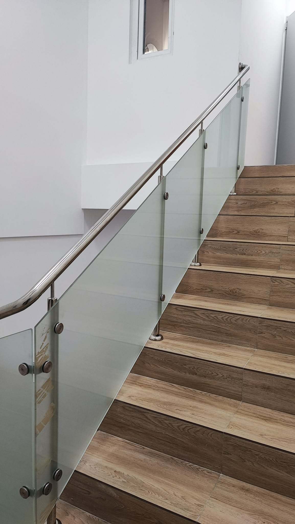 Balustradă de scară cu stâlpi din inox prinși pe trepte, rozete din inox și mână curentă rotundă din inox, cu panouri din sticlă mată