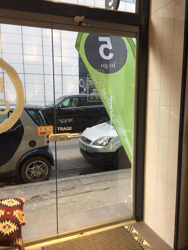 Ușă din sticlă cu profile subțiri la intrarea unui spațiu comercial, cu strada în fundal