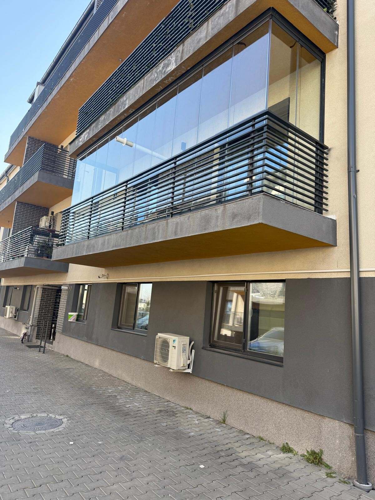 Balcon de bloc închis cu panouri de sticlă armonică, deasupra unei balustrade metalice negre