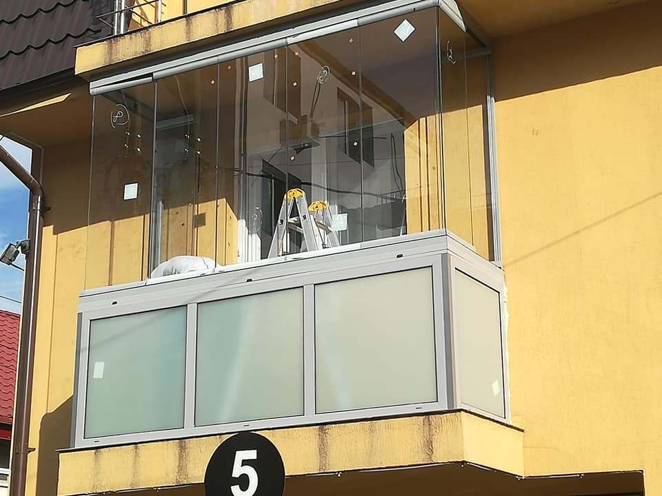 Balcon în curs de montaj cu sticlă armonică fără profile pe o fațadă galbenă