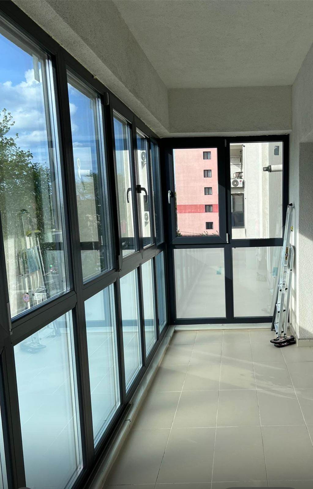 Interiorul unui balcon de bloc închis cu tâmplărie PVC antracit, cu canate sus, ochiuri fixe jos și ușă pe latura scurtă