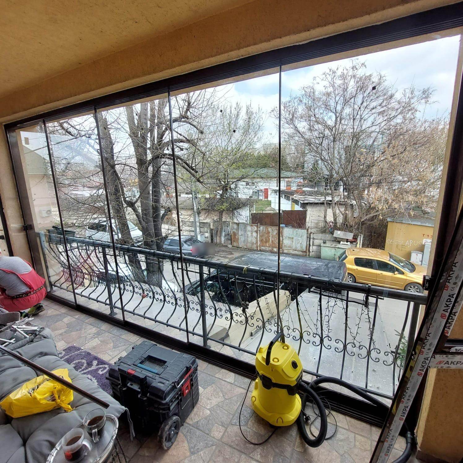 Balcon închis cu panouri mari de sticlă fără profile verticale, deasupra unei balustrade din fier forjat, cu sculele de montaj încă pe balcon