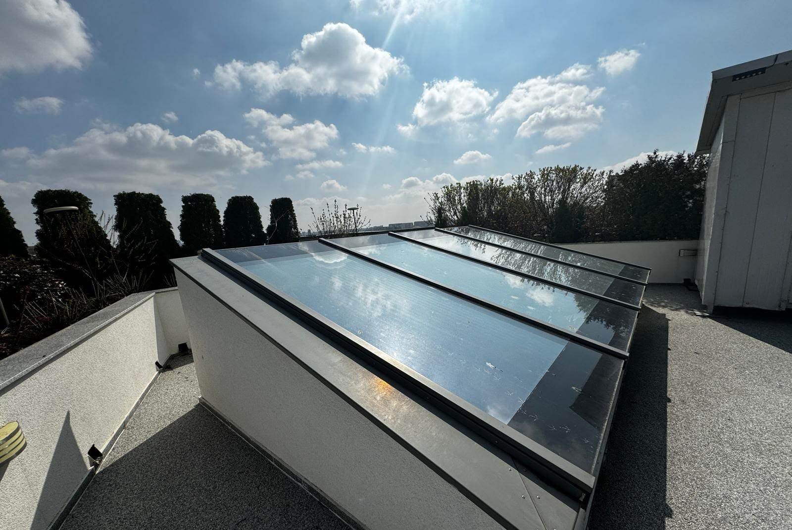 Luminator cu patru ochiuri de sticlă despărțite de profile de aluminiu gri, văzut pe diagonală, cu cerul reflectat în geam