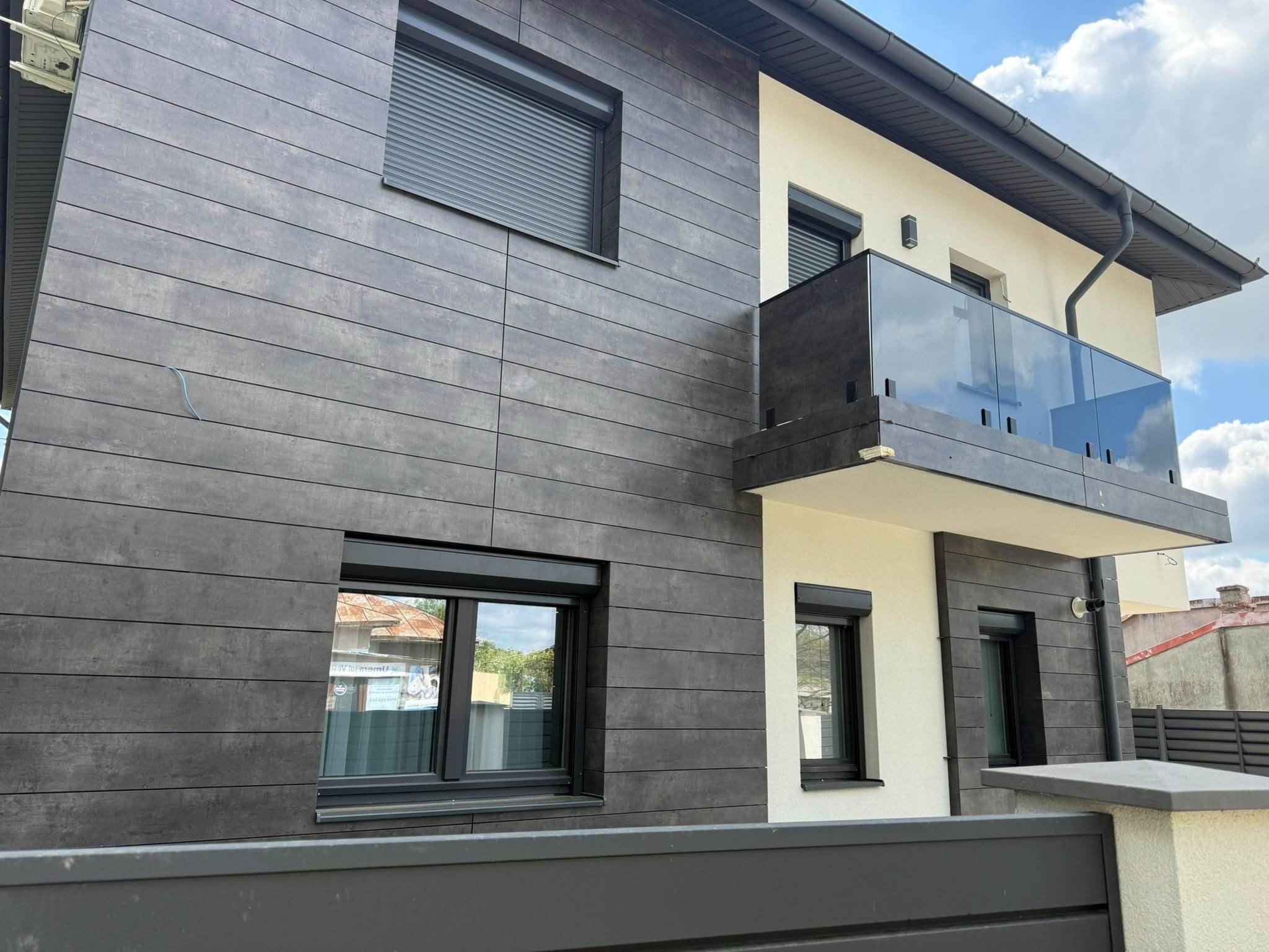 Casă nouă cu ferestre PVC antracit și rulouri exterioare cu casetă aplicată, sub un balcon cu parapet din sticlă