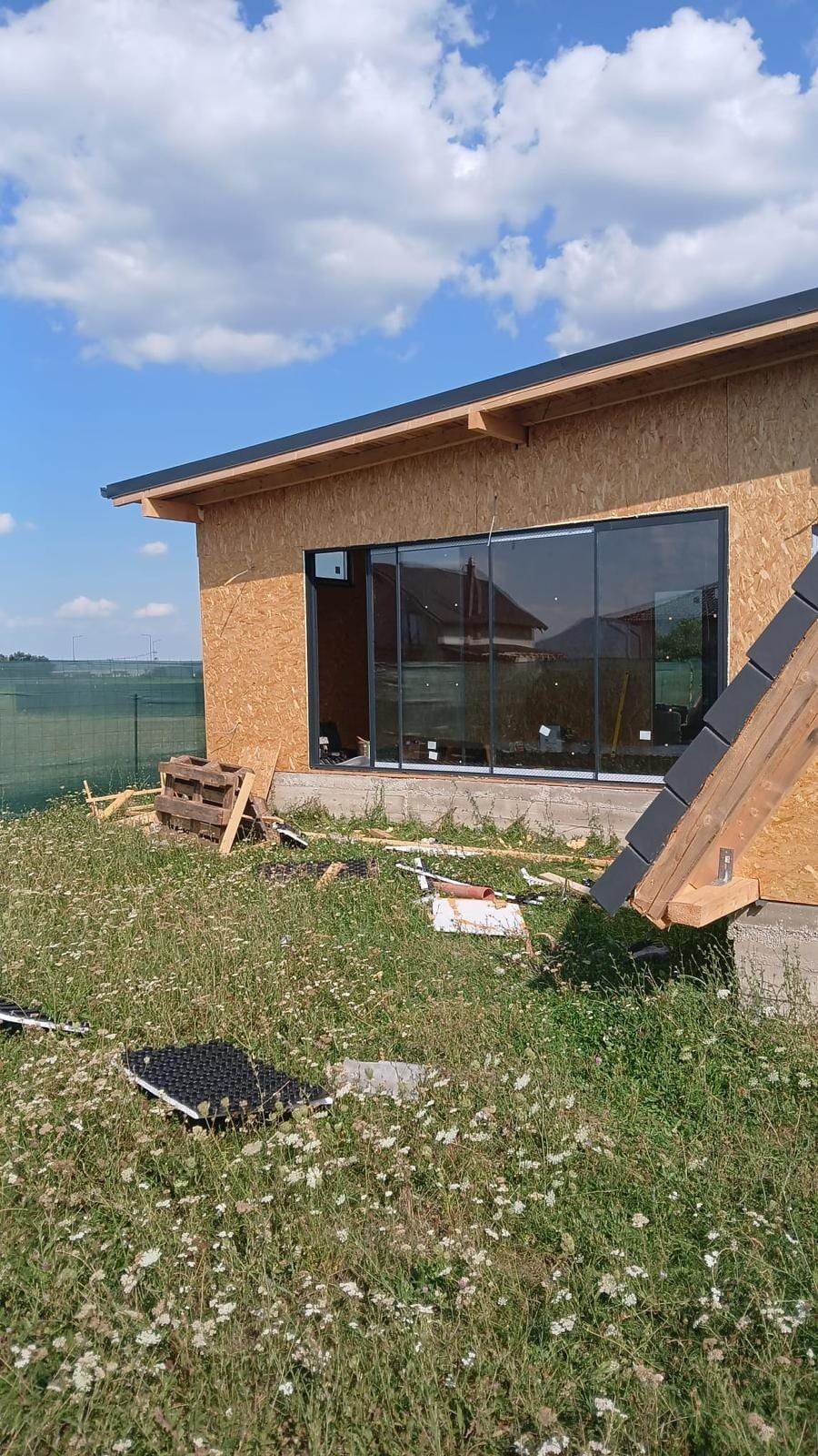 Casă în construcție din plăci OSB, cu o ușă glisantă mare cu geam termopan și profile negre spre câmp