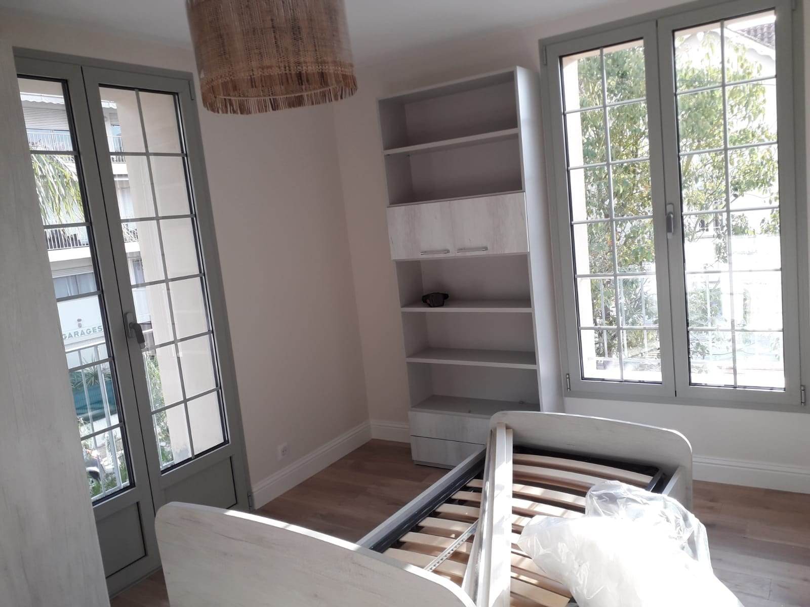 Dormitor cu o ușă franțuzească și o fereastră din aluminiu gri cu șprosuri, cu mobilierul încă în montaj