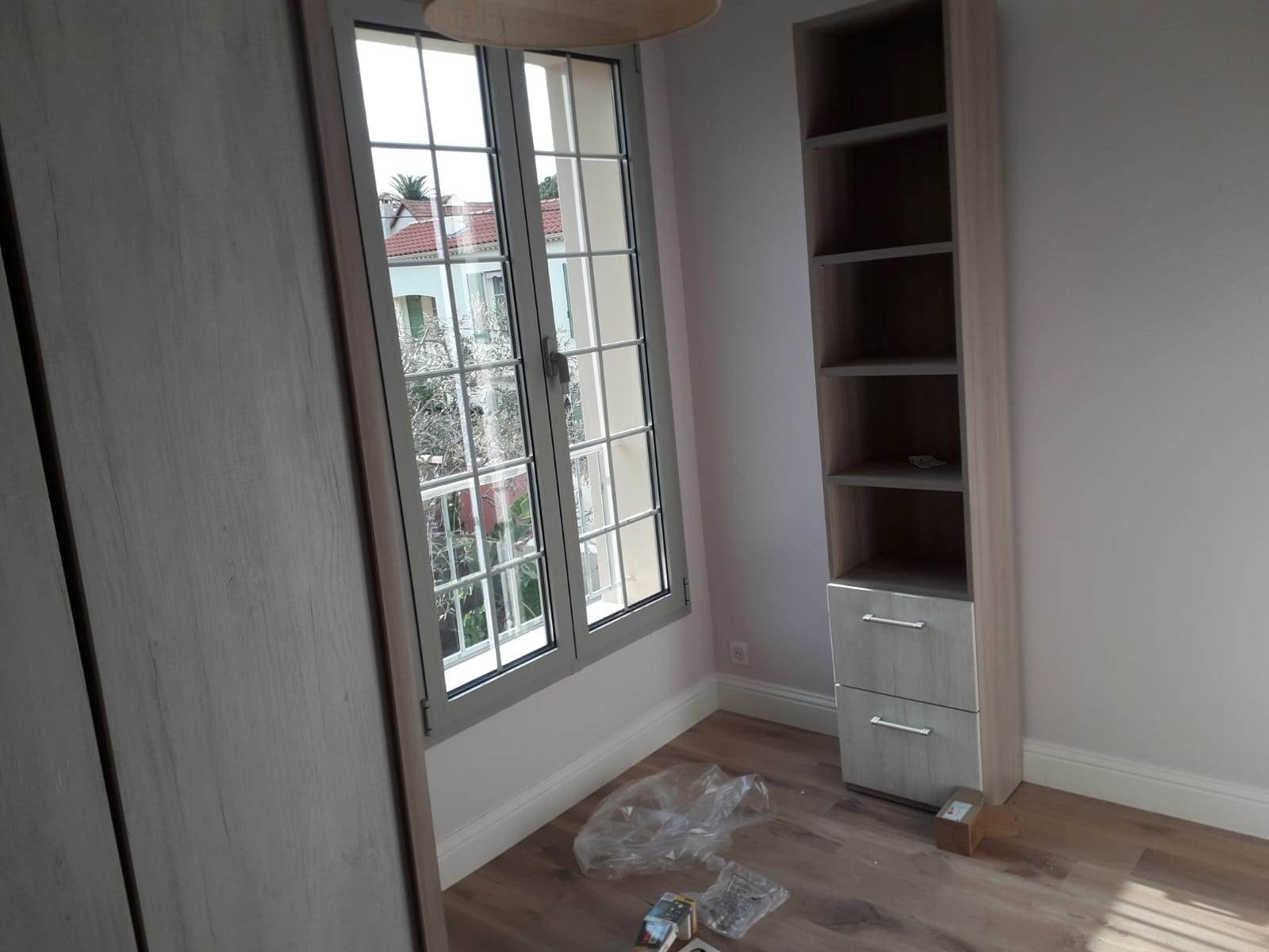 Fereastră din aluminiu gri cu șprosuri și două canate într-o cameră cu bibliotecă, cu vedere spre acoperișuri din țiglă