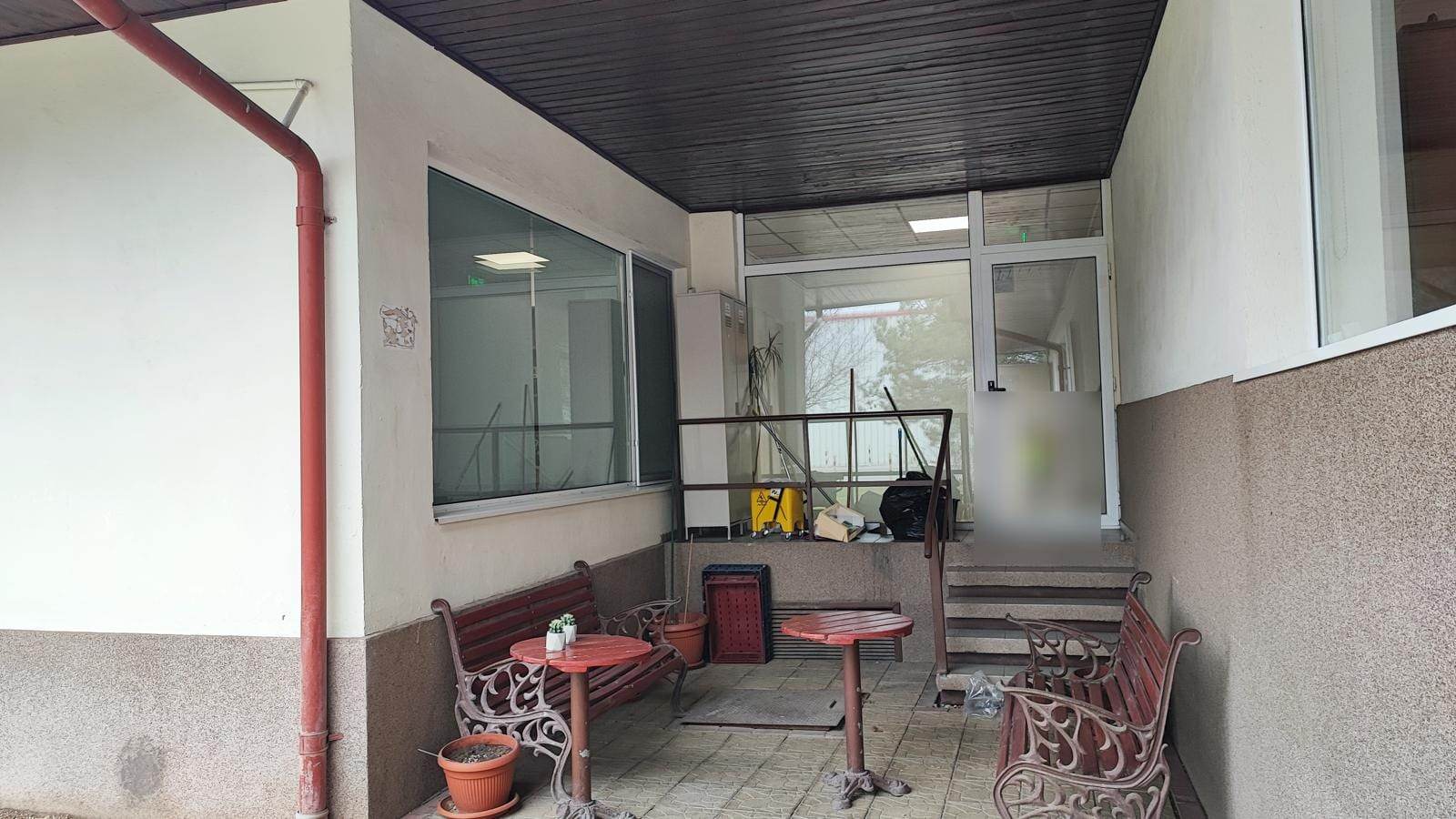Intrare laterală acoperită cu ușă albă cu geam, ferestre albe și bănci din fier forjat, la sediul Corteva România