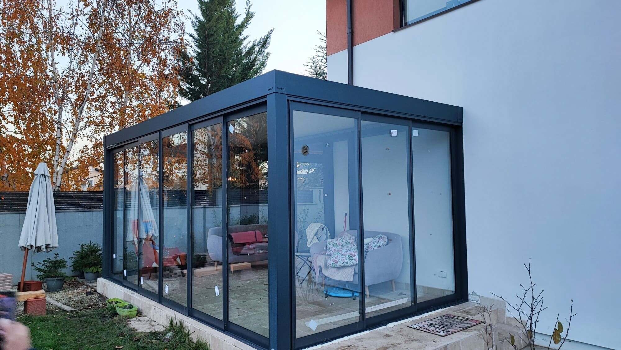 Terasă de casă din Mogoșoaia închisă complet cu panouri mari de sticlă în profile de aluminiu antracit, cu grădină în față