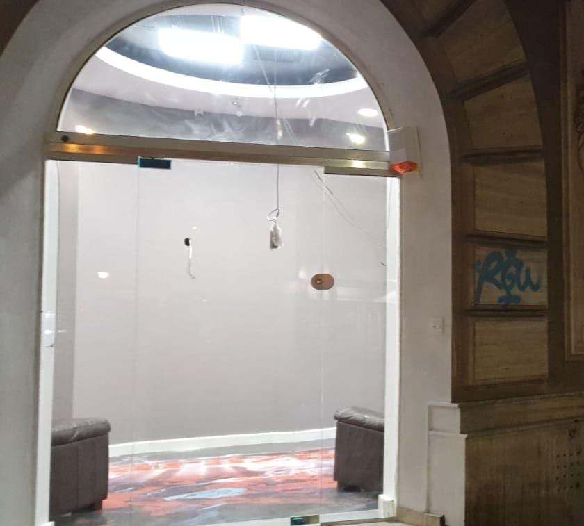 Ușă din sticlă securizată montată sub o arcadă, la intrarea unui spațiu comercial de pe Bd. Moșilor, fotografiată seara, cu interiorul luminat